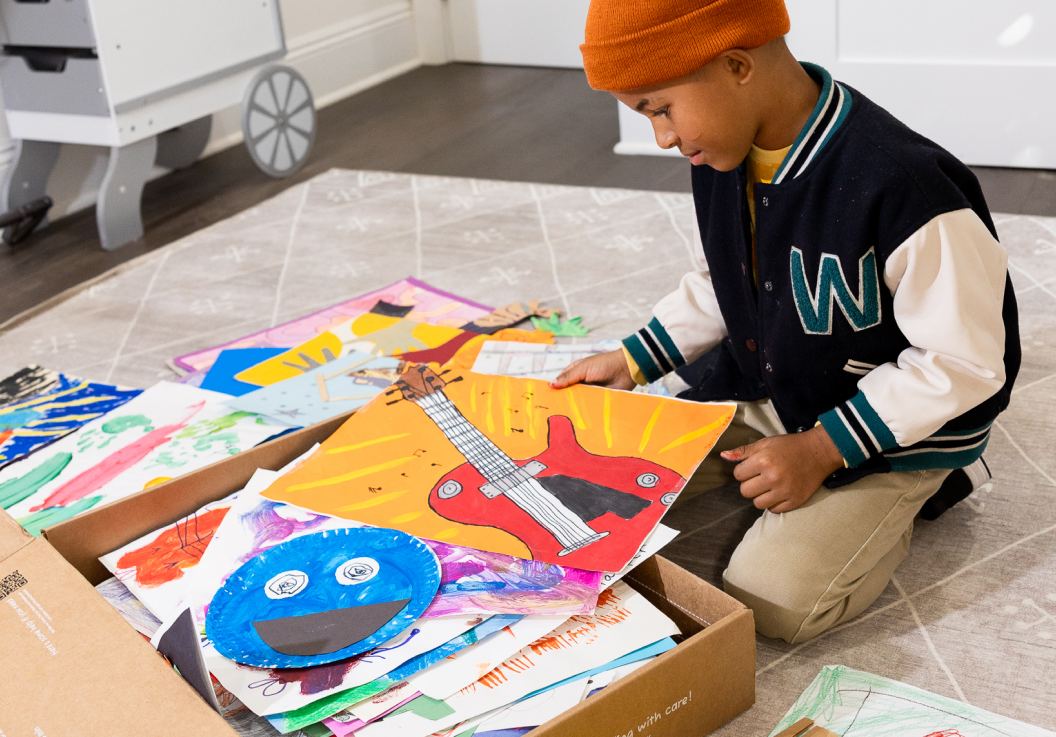 A child sorting through a box piled with drawings and paintings